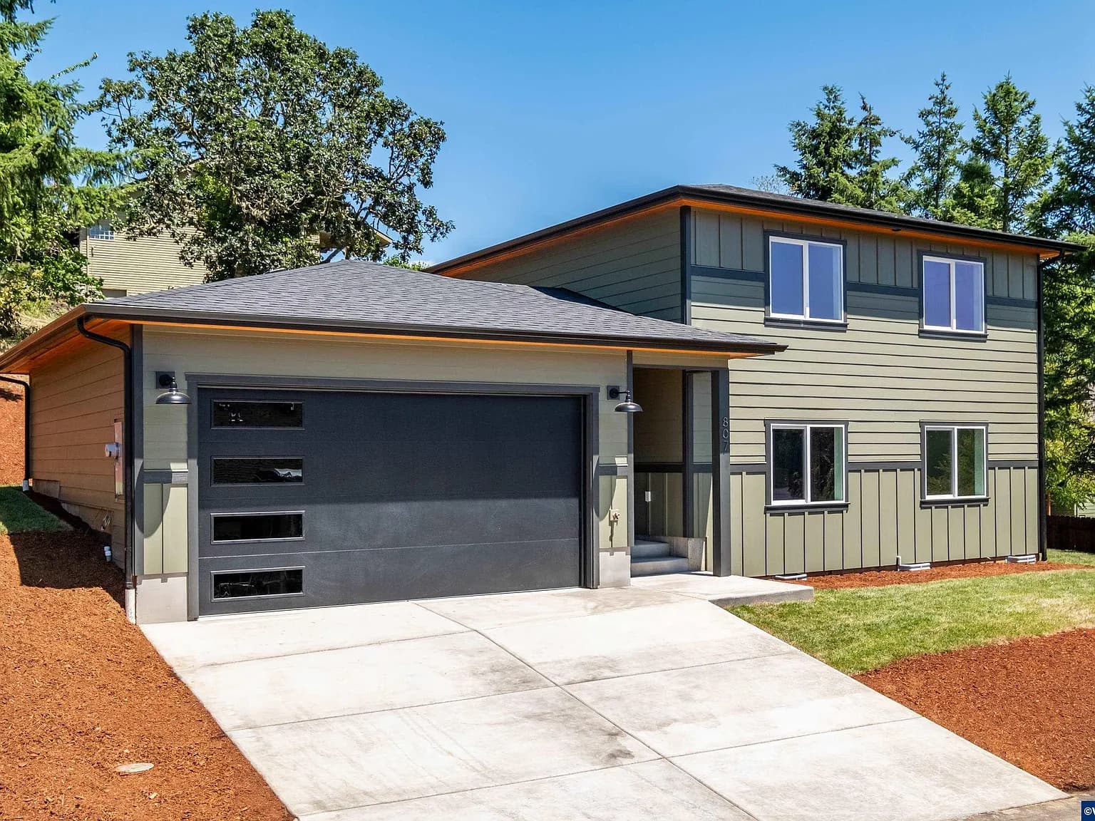 Front elevation of the Sage House, a two-story home with sage siding and a dark garage door